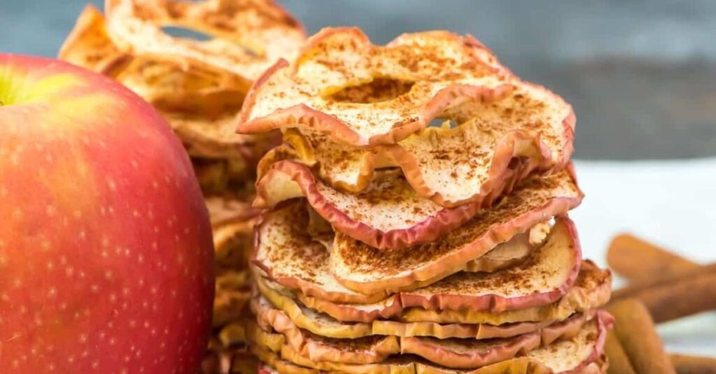 Crispy apple chips on a plate next to creamy cinnamon yogurt dip