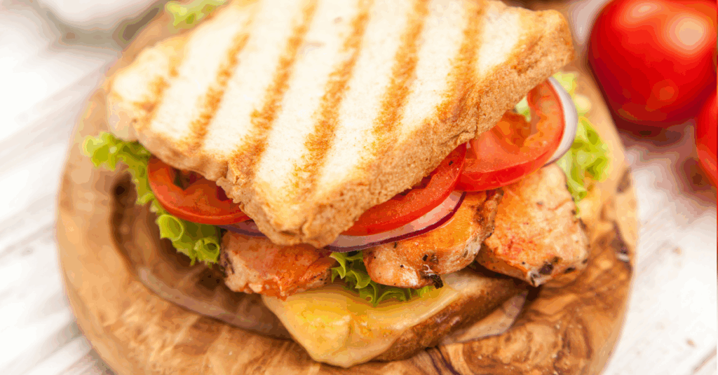 Grilled chicken bacon ranch club sandwich with tomato, lettuce, and melted cheese on toasted low-calorie bread.