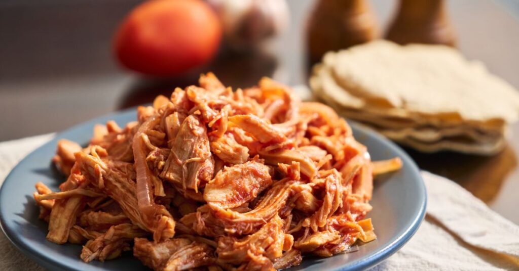 Shredded salsa chicken in slow cooker with bright red tomato sauce.