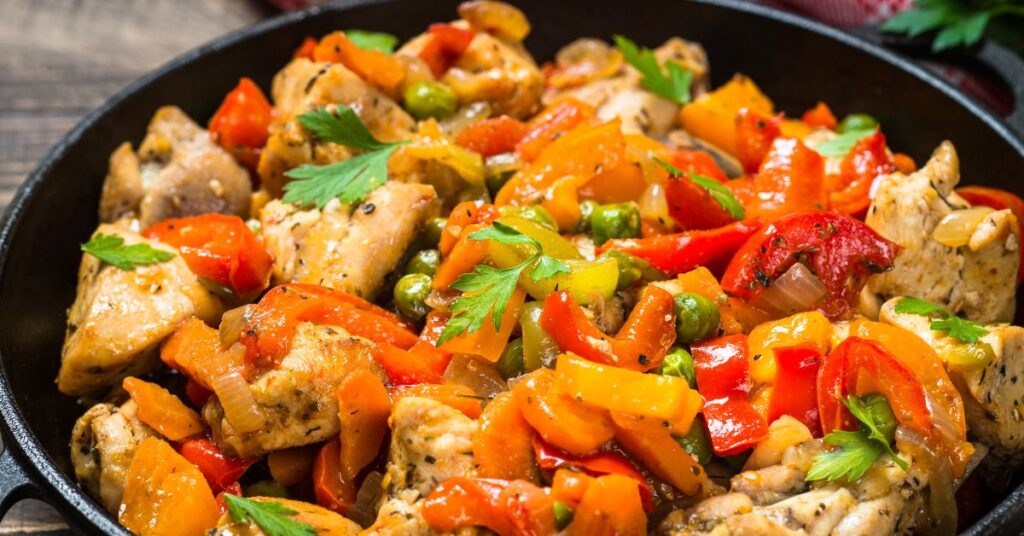 Chicken stir-fry with colorful veggies over cauliflower rice in a black bowl.