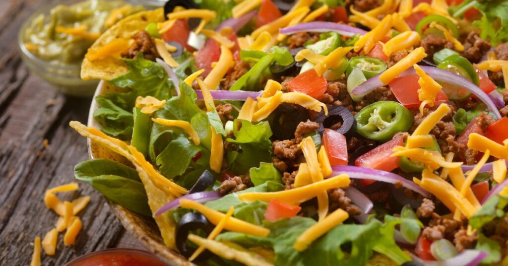 Frito taco salad topped with turkey, cheese, lettuce, onion, and Greek yogurt in a bowl.