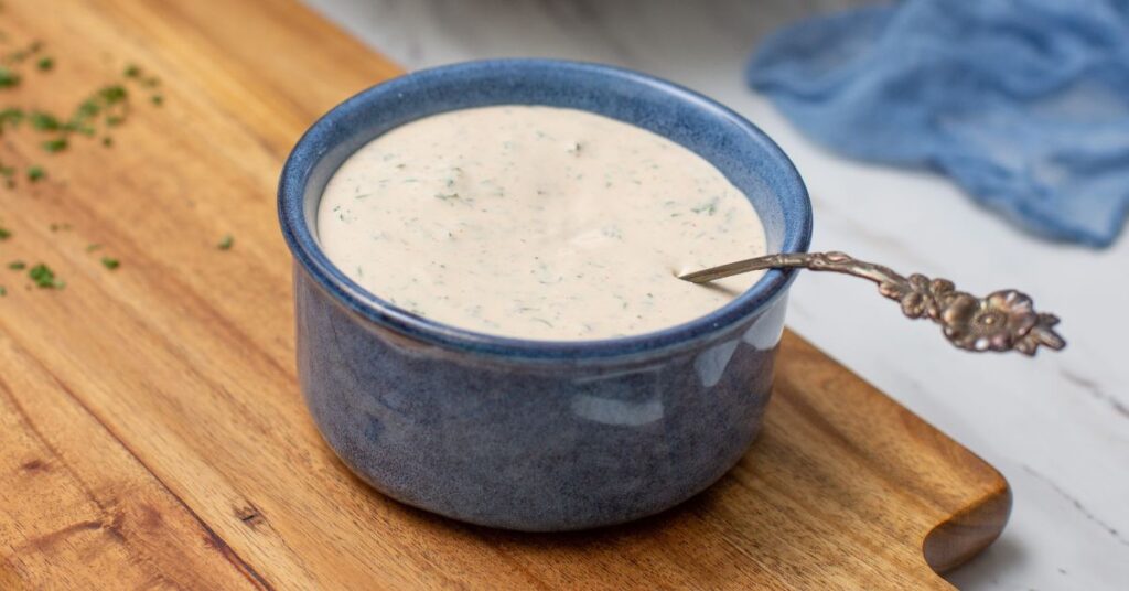 Bowl of homemade Weight Watchers Ranch dressing with a spoon and herbs